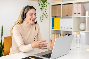 Young adult woman using laptop application talking to client in customer service department....