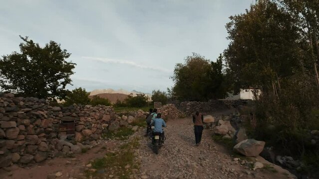 drone follows two motorbikes going trough a dirt road in a village  in the middle of the Himalaya mountains during sunset
