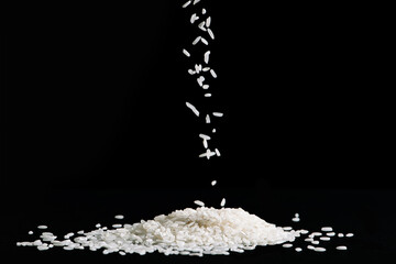 Raw white rice is falling on table. Pile of uncooked long rice on black background. Natural organic vegan food.