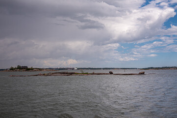 Helsinki, Finland - July 19, 2022: bare and flat Rocky Pikkuluoto Islet in front of port in gray sea water under rainy cloudscape. Boat traffic in back