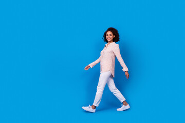 Fototapeta na wymiar Full body profile portrait of charming pretty lady walking empty space isolated on blue color background