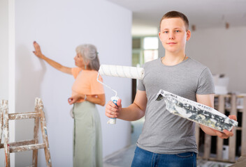 Portrait of positive teenage boy engaged in home improvement and renovation, standing on indoor...