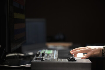 man's hand playing on a midi controller keyboard in a home recording studio
