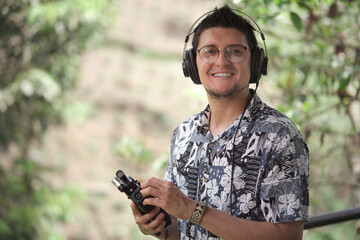 portrait of latin man while capturing audio in the wild with portable recording equipment