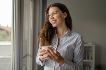 one caucasian woman hold cup of coffee while stand at the window