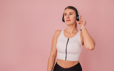 Fitness woman. Photo with copy space. Girl is listening music from white headphones against pink background