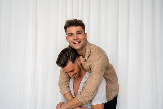 Gay couple hugging from behind  with white curtain background