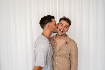 Beautiful Gay couple kissing on cheek and smiling  with white curtain background