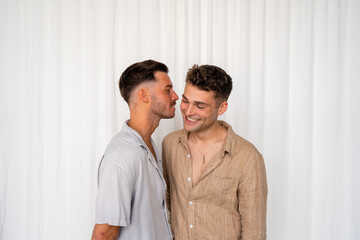 Beautiful Gay couple about to kiss on cheek and smiling  with white curtain background