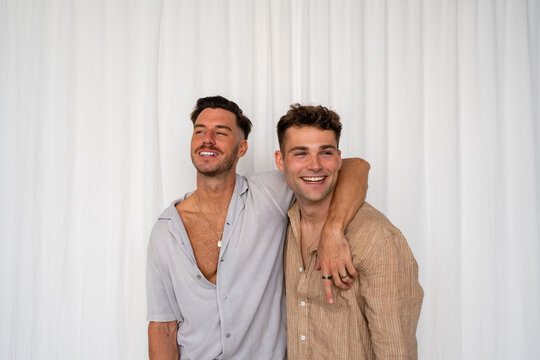 Beautiful Gay couple arm around shoulder  and smiling with white curtain background