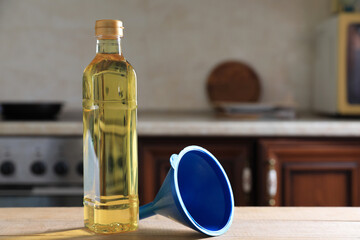 Bottle of cooking oil and funnel on wooden table in kitchen