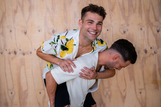 Beautiful Gay couple piggy backing with wooden background