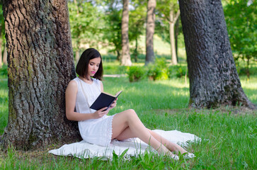 Young woman sitting in the forest and reading book on a beautiful summer day
