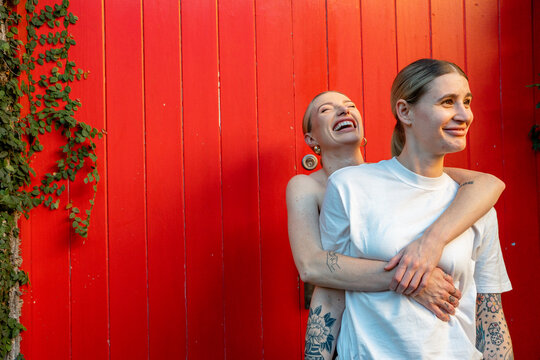 lesbian couple laughing in front of red wall 