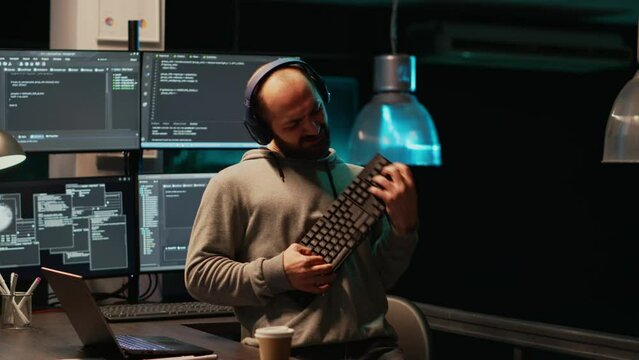 Programmer being happy and playing air guitar with keyboard instrument, enjoying music or song and having fun. Young cheerful adult acting silly fooling around late at night in office.