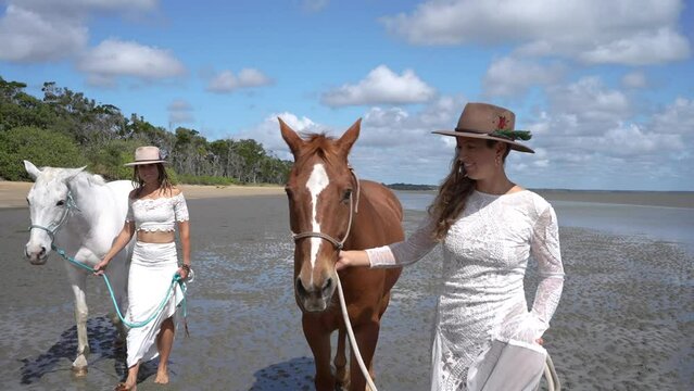 country lesbian brides walking horses on beach on wedding day