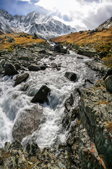 Rough mountain stream, autumn view, snow in the mountains and the sun