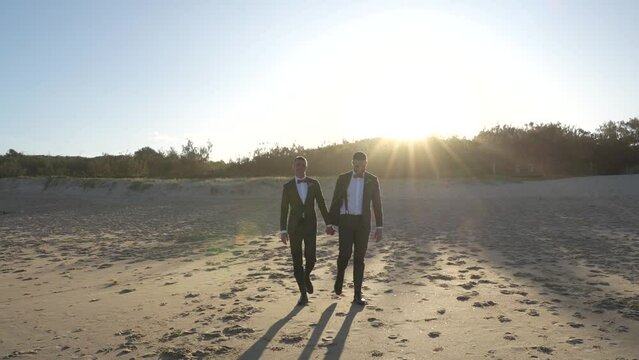 gay groom couple walking on beach on wedding day at sunset