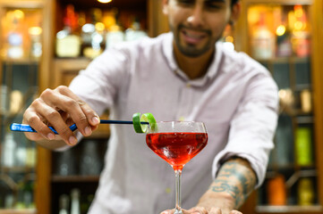 close-up of glass with red drink that barman accurate decorate with orange peel