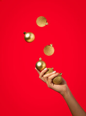 Woman's hand juggling golden Christmas baubles on red background. Minimal holiday concept. Happy New Year. Copy space.