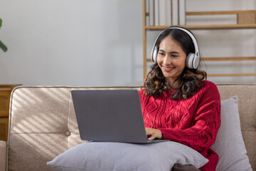 Beautiful Young Asian  indian woman using digital tablet laptop while headphones sitting on sofa at home, Use technology, lifestyle concept.
