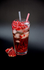Tall glass of pomegranate juice with ice and straws on a black background.