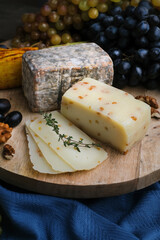 Still life of Cheese plate assortment. Fruits, knife and nuts with different cheese on wooden board. Camembert, Tom, soft and hard cheeses.