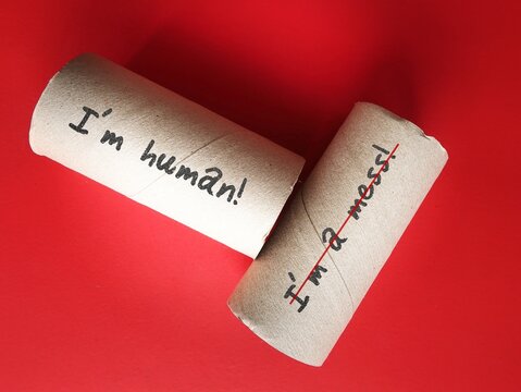 Toilet paper rolls on red background with handwriting I AM A MESS, changed to I AM HUMAN - to overcome negative self talk or inner voice critic, change to positive thought to boos self esteem