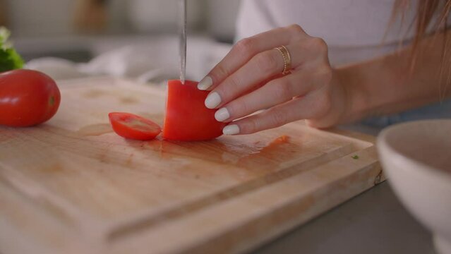 Close up of female hand slicing tomato with kitchen knife