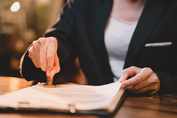 A seal to show approval of an agreement or contract by an authorized person. A businesswoman is about to stamp a document at the office legally. The boss signs the certificate or letter on the desk.