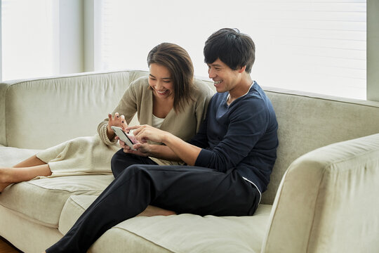 ソファでスマホを見て笑う夫婦