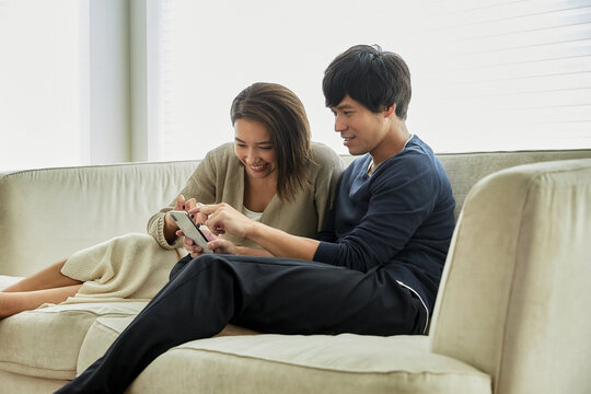 ソファでスマホを見て笑う夫婦