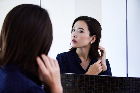 鏡の前でピアスをつける30代女性