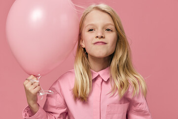 Fototapeta na wymiar joyful school-age girl stands on a pink background with a big balloon in her hand and smiles broadly while looking at the camera. Horizontal photo with blank space for advertising layout insert