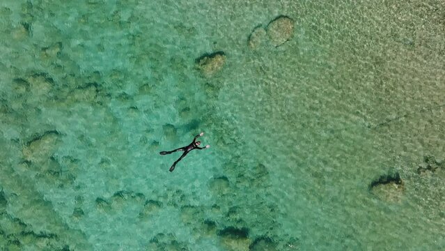 Twisting top down aerial of snorkeler on back in crystal clear ocean