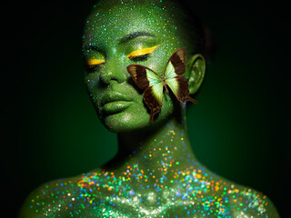 Fashion model woman skin face in bright sparkles with green butterfly colorful neon lights, beautiful girl sexy lips. Glowing art green skin make-up. Glitter metallic shine silver green makeup