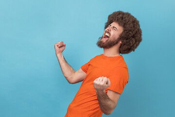 Side view of excited positive happy man with Afro hairstyle wearing orange T-shirt screaming for...