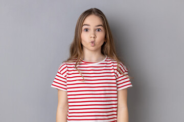 Funny surprised little girl wearing striped T-shirt making fish face with pout lips and looking...