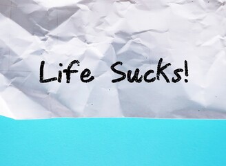 Crumpled paper on blue background with handwritten text LIFE SUCKS, saying when things are not...