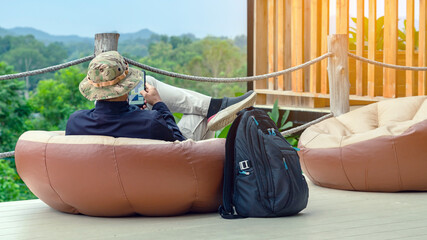 Male tourist wear hat with face mask with backpack use tablet while sit to relax on large cushions...