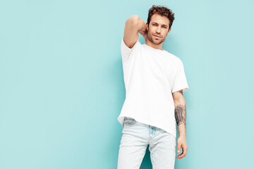 Portrait of handsome confident stylish hipster lambersexual model. Sexy man dressed in white T-shirt and jeans. Fashion male isolated on blue wall in studio. Mockup