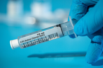 medical syringe with sodium chloride in a doctor's hand on a blue background - obrazy, fototapety, plakaty