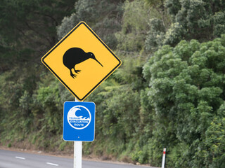 Two road signs on a New Zealand road.One warns to look out for kiwi's with a silhouetted bird...