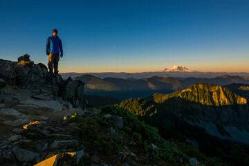 Athletic adventurous male hiker standing on top of a mountain with Mount Rainier in the background...