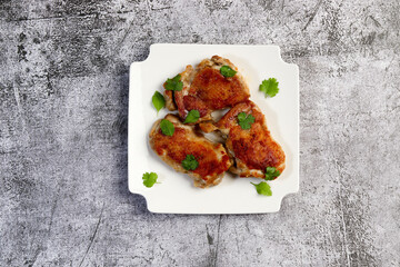 Crispy skin chicken Tapaka thighs with herbs on a white square  plate on a dark background. Top view, flat lay