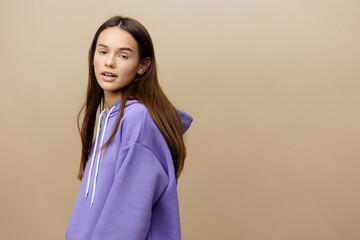 Fototapeta premium Horizontal photo of a pleasant, calm, relaxed woman standing sideways to the camera in a purple suit on a beige background