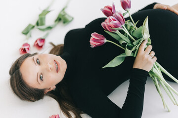 Beautiful pregnant woman with flowers lies on a white background, top view. The concept of conscious fatherhood, happy motherhood and easy pregnancy.