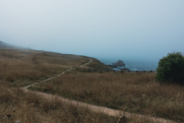 Obraz premium A path for walking along the blue ocean with a rocky shore in the fog. Picturesque weather and nature.
