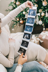 A couple in love holds an ultrasound in their hands against the background of a Christmas tree. The concept of conscious parenthood, happy motherhood and easy pregnancy.