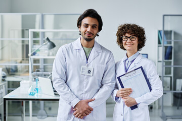 Two young clinicians or chemists in labcoats standing in front of camera in scientific laboratory...